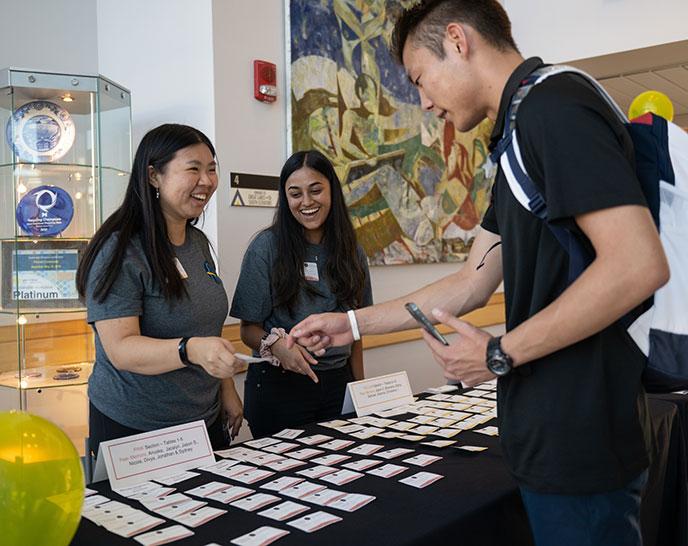 Two students handing out name tags and helping another student