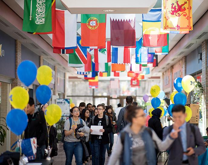 Students walking through a hallway in Pierpont Commons with flags from different countries hanging overhead