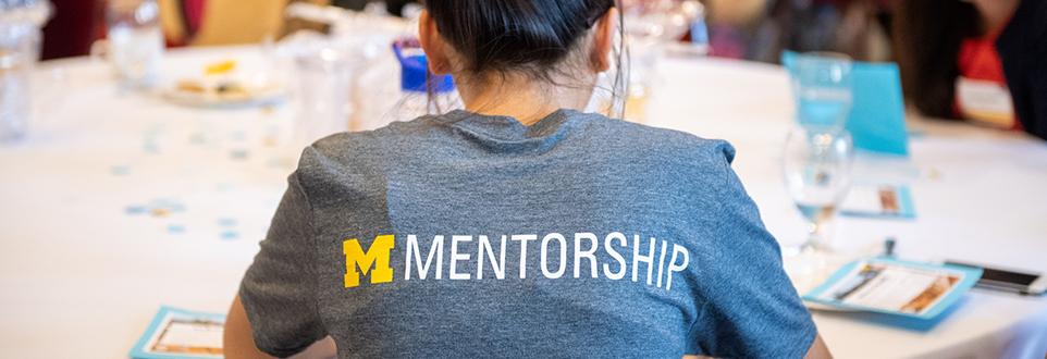 Girl at table wearing a mentorship t-shirt