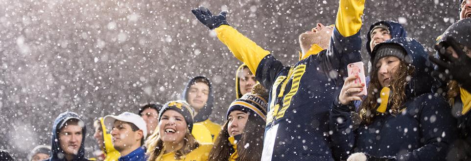 Students cheering at football game while it is snowing